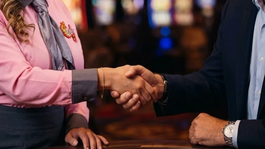 Asesora del casino estrechando la mano de un cliente sobre una mesa de juego